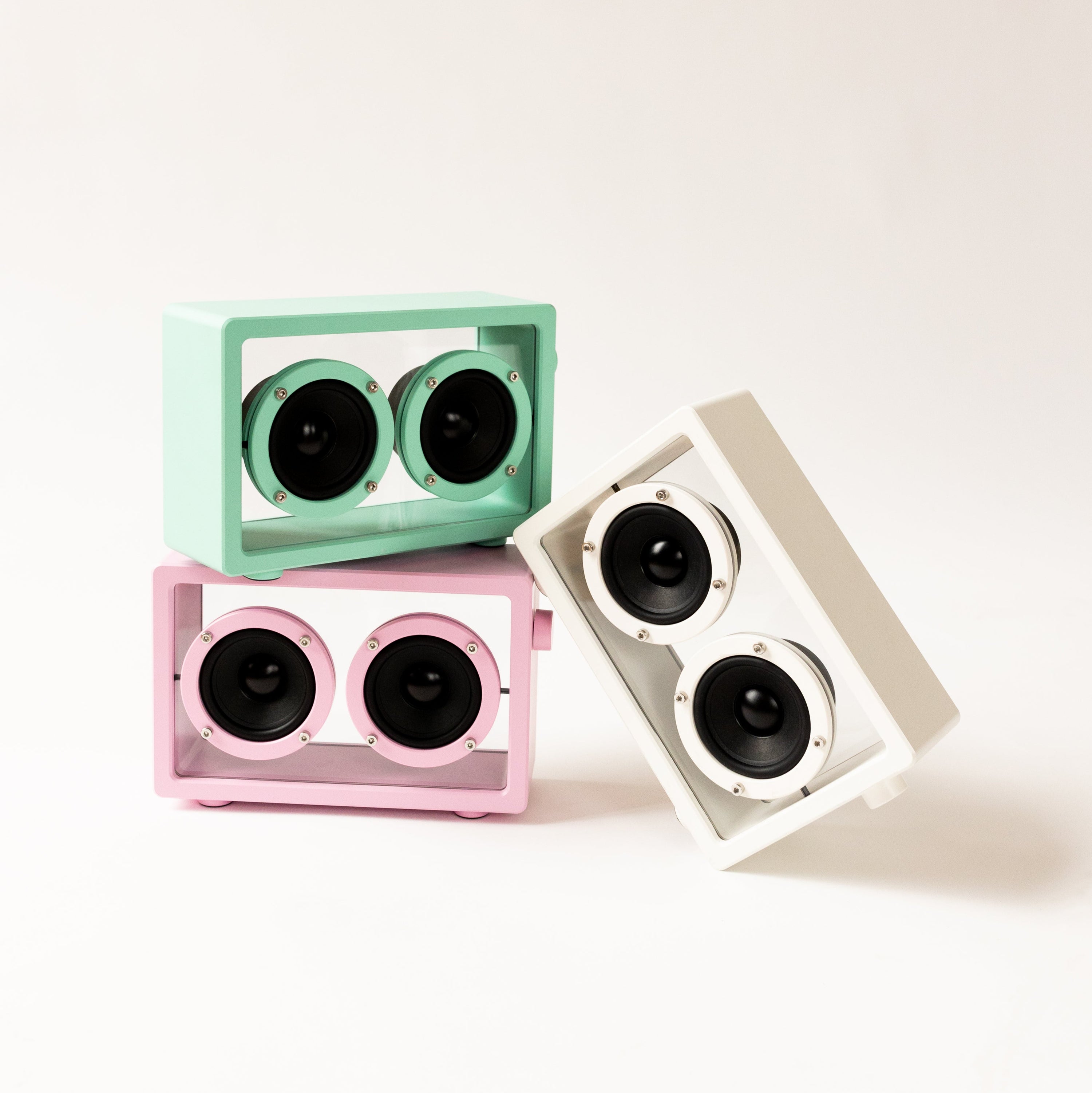 Three small speakers in green, pink, and white on a white background