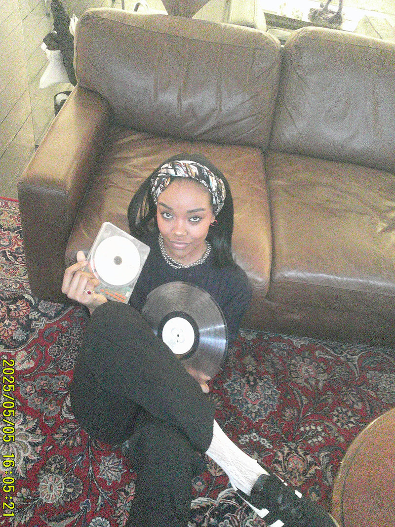 Person holding vinyl records on a patterned rug with a brown couch.
